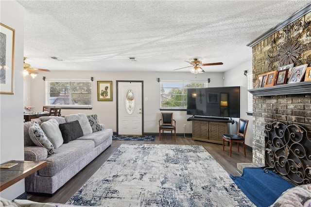 living room featuring dark wood-type flooring, a textured ceiling, ceiling fan, and a brick fireplace