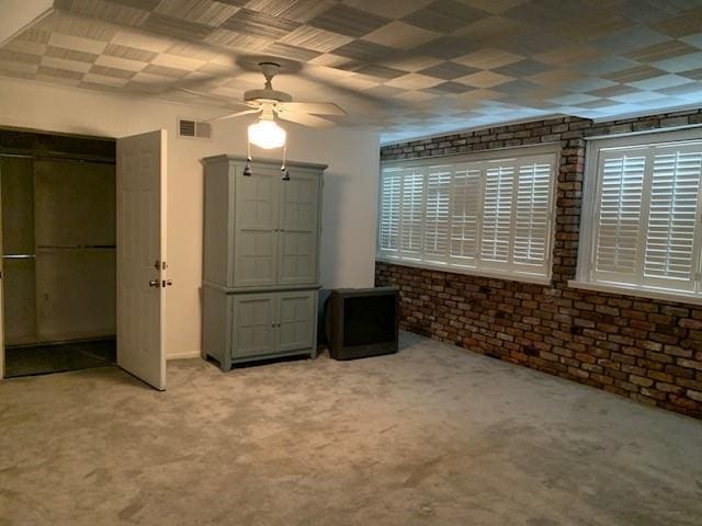 unfurnished bedroom featuring light carpet, ceiling fan, and brick wall