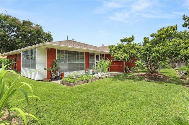 rear view of property with a garden, a lawn, and brick siding