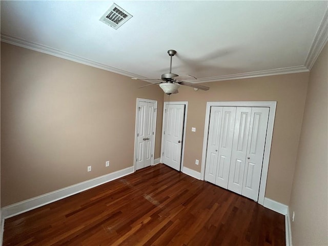 unfurnished bedroom featuring hardwood / wood-style flooring, two closets, crown molding, and ceiling fan