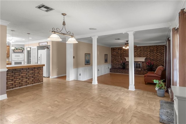 living room with decorative columns, ceiling fan, brick wall, a fireplace, and ornamental molding