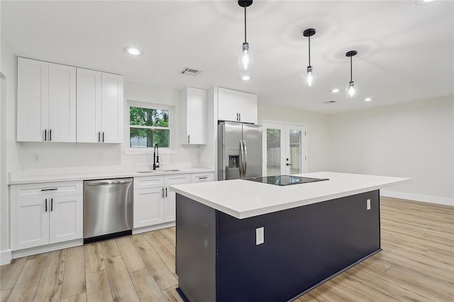 kitchen featuring white cabinets, stainless steel appliances, decorative light fixtures, and light hardwood / wood-style flooring