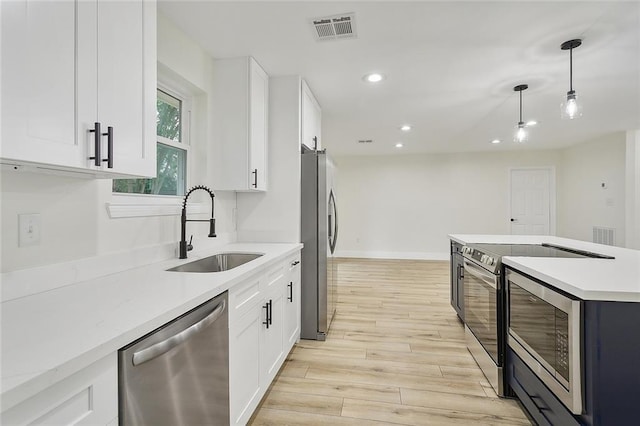 kitchen with white cabinetry, decorative light fixtures, stainless steel appliances, sink, and light hardwood / wood-style flooring