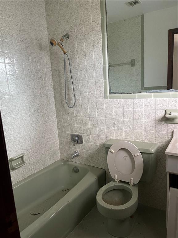 full bathroom featuring tile walls, vanity, tiled shower / bath, and toilet