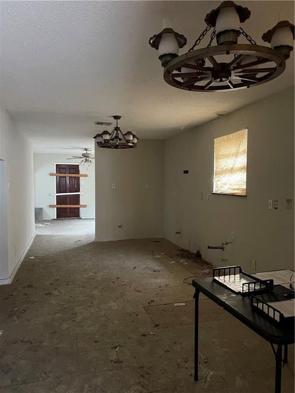 unfurnished dining area featuring ceiling fan with notable chandelier and a textured ceiling