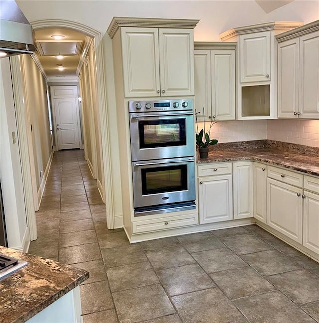 kitchen with backsplash, double oven, and dark stone countertops