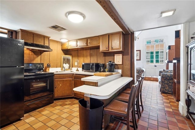 kitchen featuring kitchen peninsula, a breakfast bar, sink, black appliances, and beamed ceiling