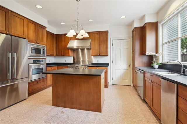 kitchen with appliances with stainless steel finishes, pendant lighting, a notable chandelier, a kitchen island, and range hood