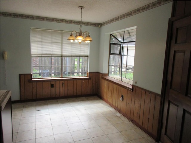 unfurnished dining area featuring a chandelier, wooden walls, and a textured ceiling