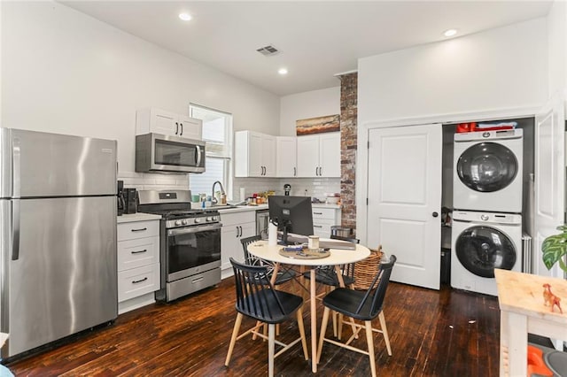 kitchen with decorative backsplash, stainless steel appliances, white cabinets, stacked washer and dryer, and dark hardwood / wood-style floors