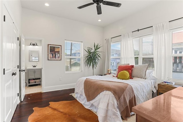 bedroom featuring multiple windows, connected bathroom, ceiling fan, and dark wood-type flooring