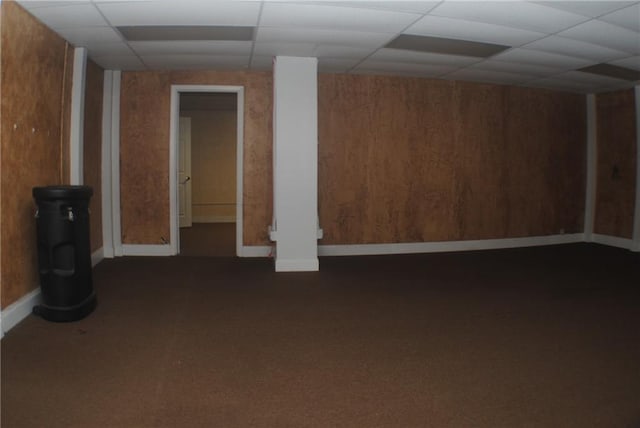 basement featuring a drop ceiling, wood walls, and dark carpet