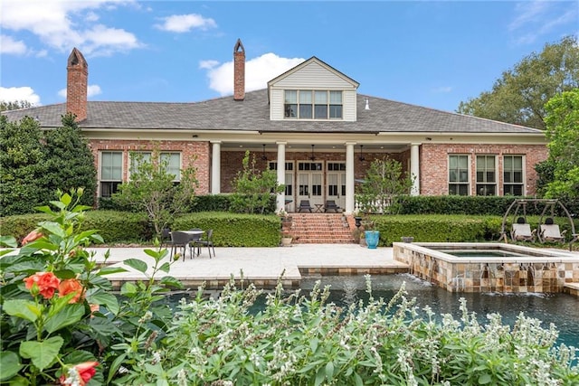 rear view of property featuring brick siding, an in ground hot tub, and a patio