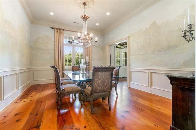 dining room with wood-type flooring, an inviting chandelier, crown molding, and a decorative wall