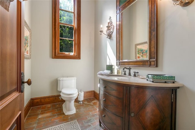 bathroom featuring vanity, brick floor, toilet, and baseboards