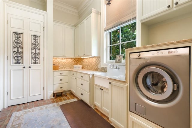 laundry area featuring crown molding, washer / dryer, brick floor, cabinet space, and a sink