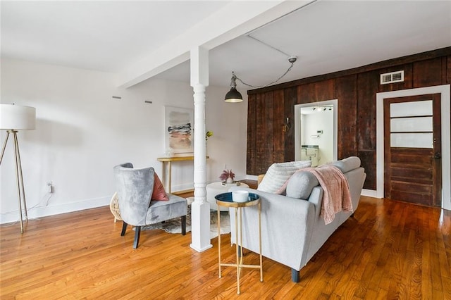 living room with beam ceiling, wooden walls, hardwood / wood-style floors, and ornate columns