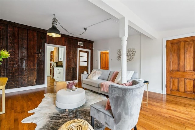 living room featuring decorative columns, wooden walls, and hardwood / wood-style flooring