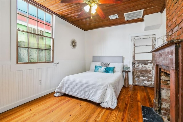 bedroom featuring wood-type flooring, a brick fireplace, wooden walls, ceiling fan, and wooden ceiling