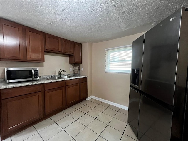 kitchen with sink, black fridge, light tile patterned floors, and a textured ceiling