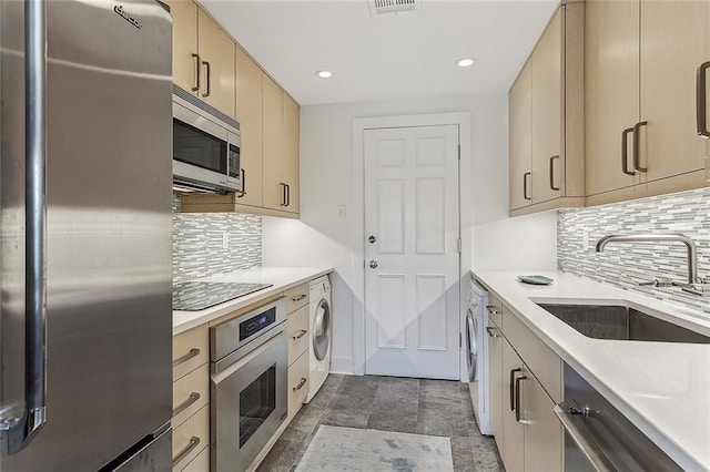 kitchen featuring backsplash, appliances with stainless steel finishes, dark tile patterned flooring, washer / dryer, and sink