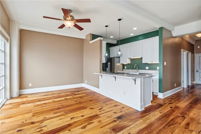 kitchen featuring a kitchen bar, ceiling fan, white cabinetry, light hardwood / wood-style flooring, and stainless steel fridge