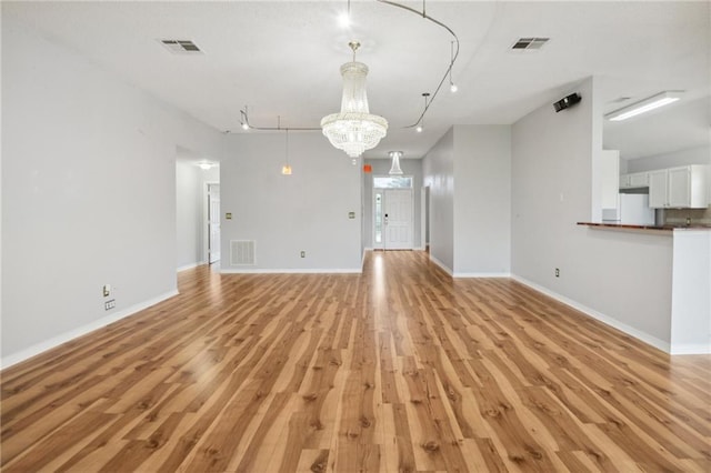 unfurnished living room featuring light hardwood / wood-style floors, track lighting, and a chandelier