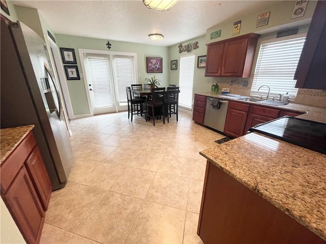 kitchen with light tile patterned floors, a textured ceiling, stainless steel appliances, light stone countertops, and sink