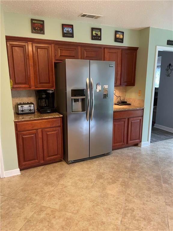 kitchen featuring light stone counters, a textured ceiling, stainless steel fridge, and light tile patterned floors