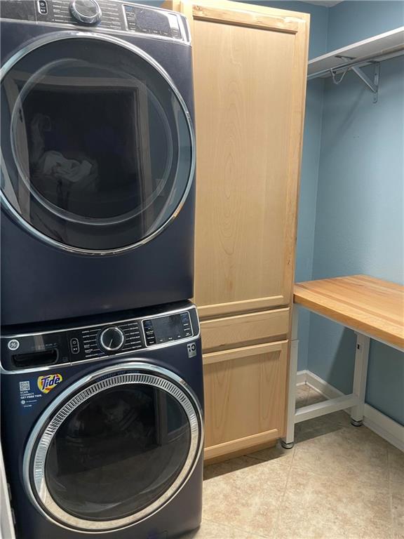 laundry area featuring stacked washer and dryer, cabinets, and light tile patterned floors