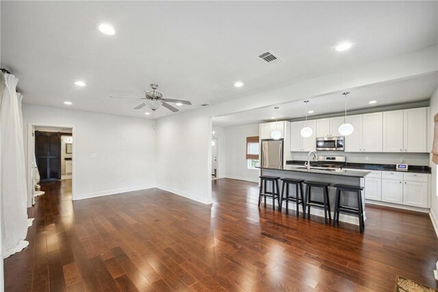 kitchen with dark wood-type flooring, ceiling fan, stainless steel appliances, and a breakfast bar area