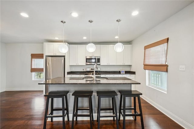 kitchen with dark stone counters, dark hardwood / wood-style flooring, an island with sink, sink, and appliances with stainless steel finishes