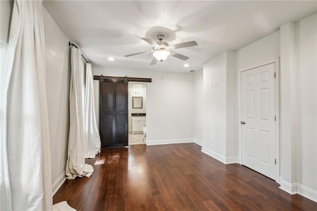 spare room featuring dark wood-type flooring, ceiling fan, and a barn door