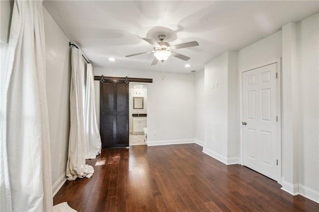 empty room with a barn door, dark hardwood / wood-style floors, and ceiling fan