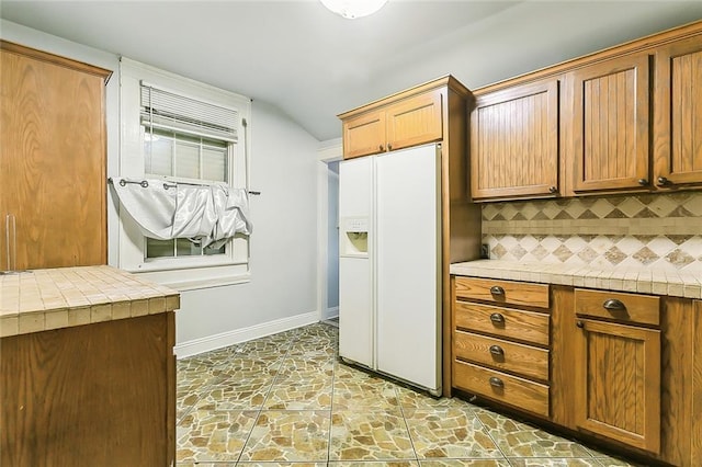 kitchen with tasteful backsplash, white refrigerator with ice dispenser, tile countertops, and lofted ceiling