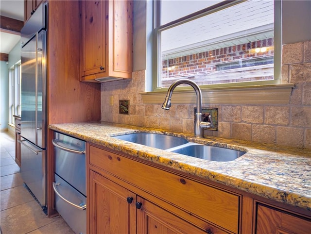 kitchen featuring stainless steel built in refrigerator, sink, decorative backsplash, light tile patterned floors, and light stone countertops