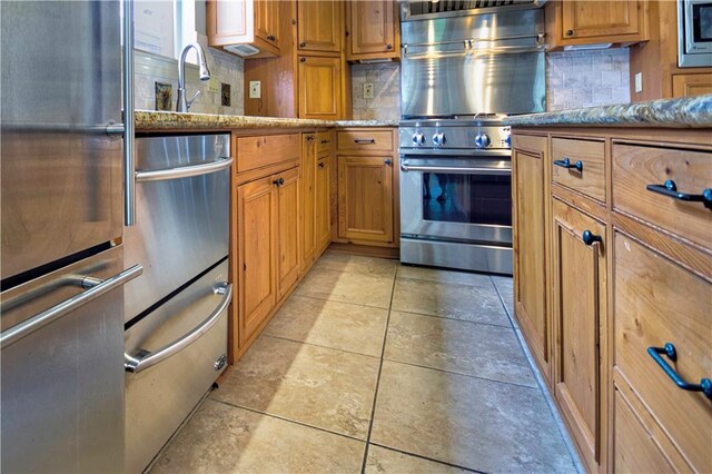 kitchen with light stone countertops, stainless steel appliances, light tile patterned floors, and decorative backsplash