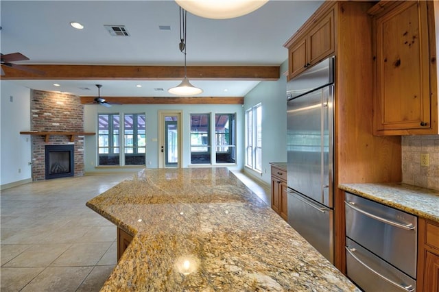 kitchen with light stone counters, beam ceiling, decorative light fixtures, stainless steel appliances, and a fireplace