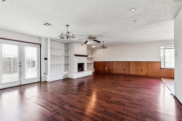 unfurnished living room featuring ceiling fan with notable chandelier, dark hardwood / wood-style floors, a fireplace, a textured ceiling, and brick wall