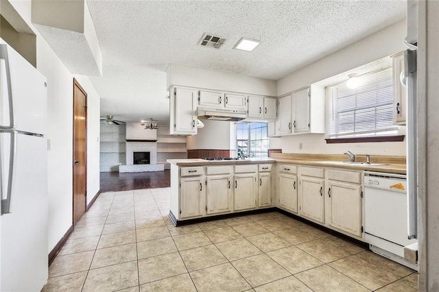 kitchen with white appliances, ceiling fan, light tile patterned floors, a fireplace, and kitchen peninsula