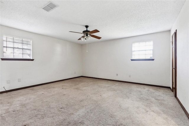 carpeted spare room featuring a textured ceiling, a wealth of natural light, and ceiling fan