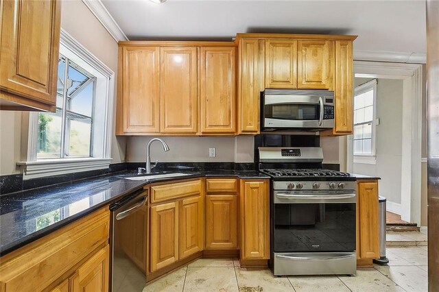 kitchen with a sink, dark stone countertops, ornamental molding, and stainless steel appliances