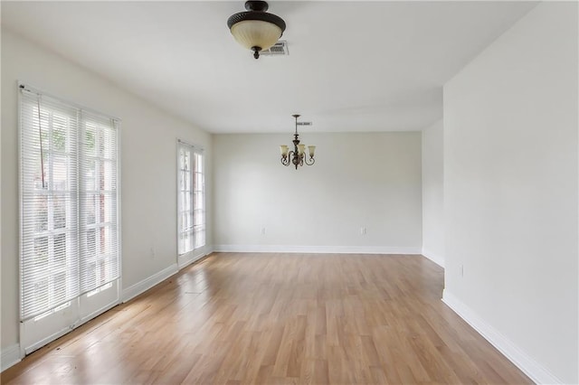 unfurnished room with a notable chandelier, a wealth of natural light, and light wood-type flooring