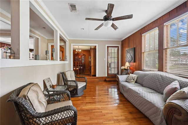 living room featuring wood walls, light hardwood / wood-style floors, ornamental molding, built in features, and ceiling fan with notable chandelier