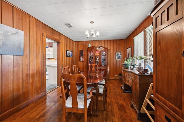 dining area with wooden walls, an inviting chandelier, and dark wood-type flooring