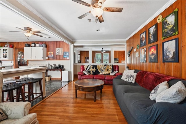 living room featuring wood walls, ceiling fan, crown molding, and wood-type flooring