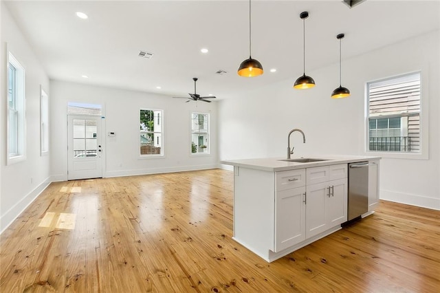 kitchen featuring white cabinets, sink, decorative light fixtures, light hardwood / wood-style floors, and an island with sink