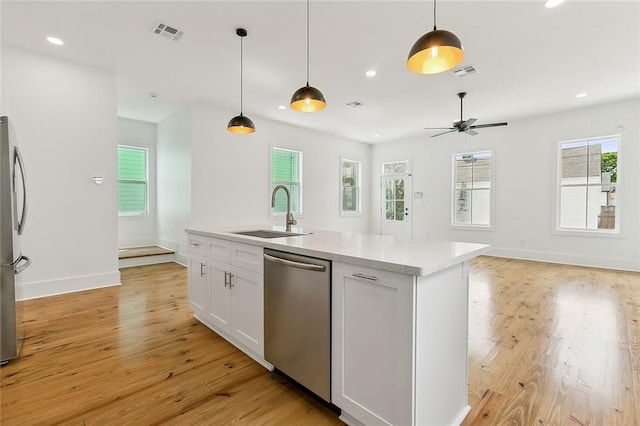 kitchen featuring light hardwood / wood-style flooring, stainless steel appliances, hanging light fixtures, a kitchen island with sink, and white cabinetry