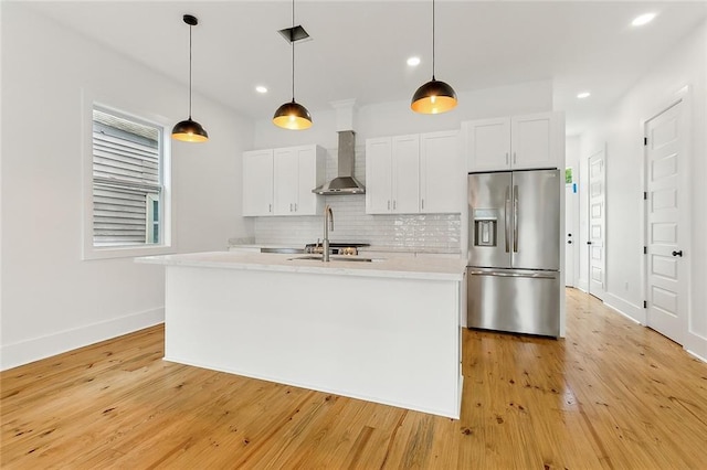 kitchen featuring a kitchen island with sink, light hardwood / wood-style flooring, stainless steel refrigerator with ice dispenser, and wall chimney exhaust hood