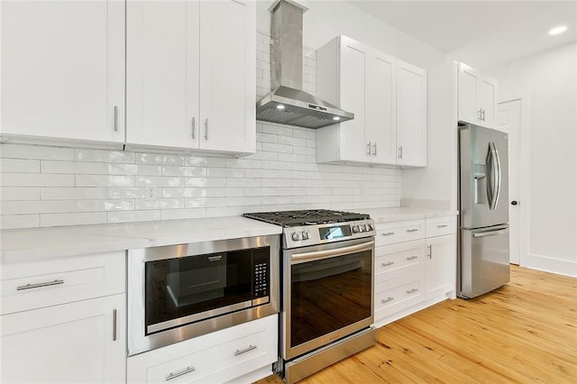 kitchen with light hardwood / wood-style flooring, tasteful backsplash, wall chimney range hood, white cabinets, and appliances with stainless steel finishes